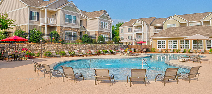 a pool with chairs and umbrellas in front of apartment buildings